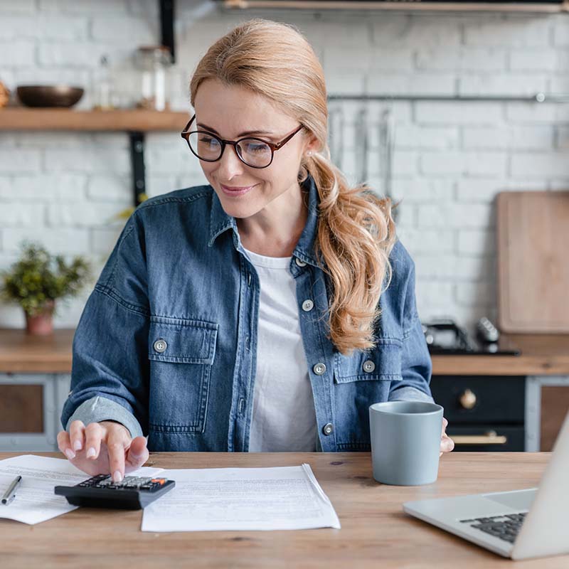 Young woman sitting at a kitchen desk, checking her calculator 